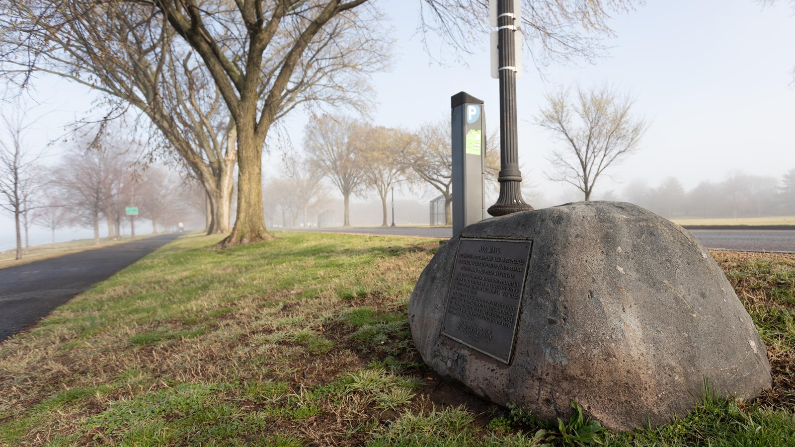 A stone marker inscribed with words sites on a pathway surrounded by foggy trees. 