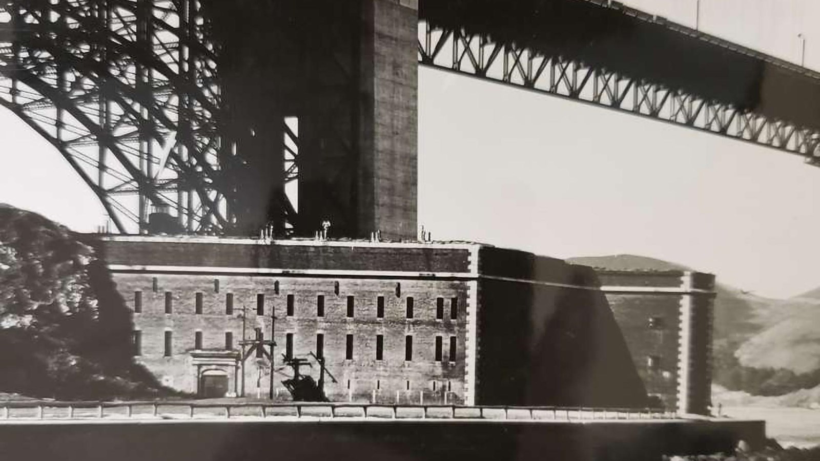 A black and white image of Fort Point beneath the Golden Gate Bridge.