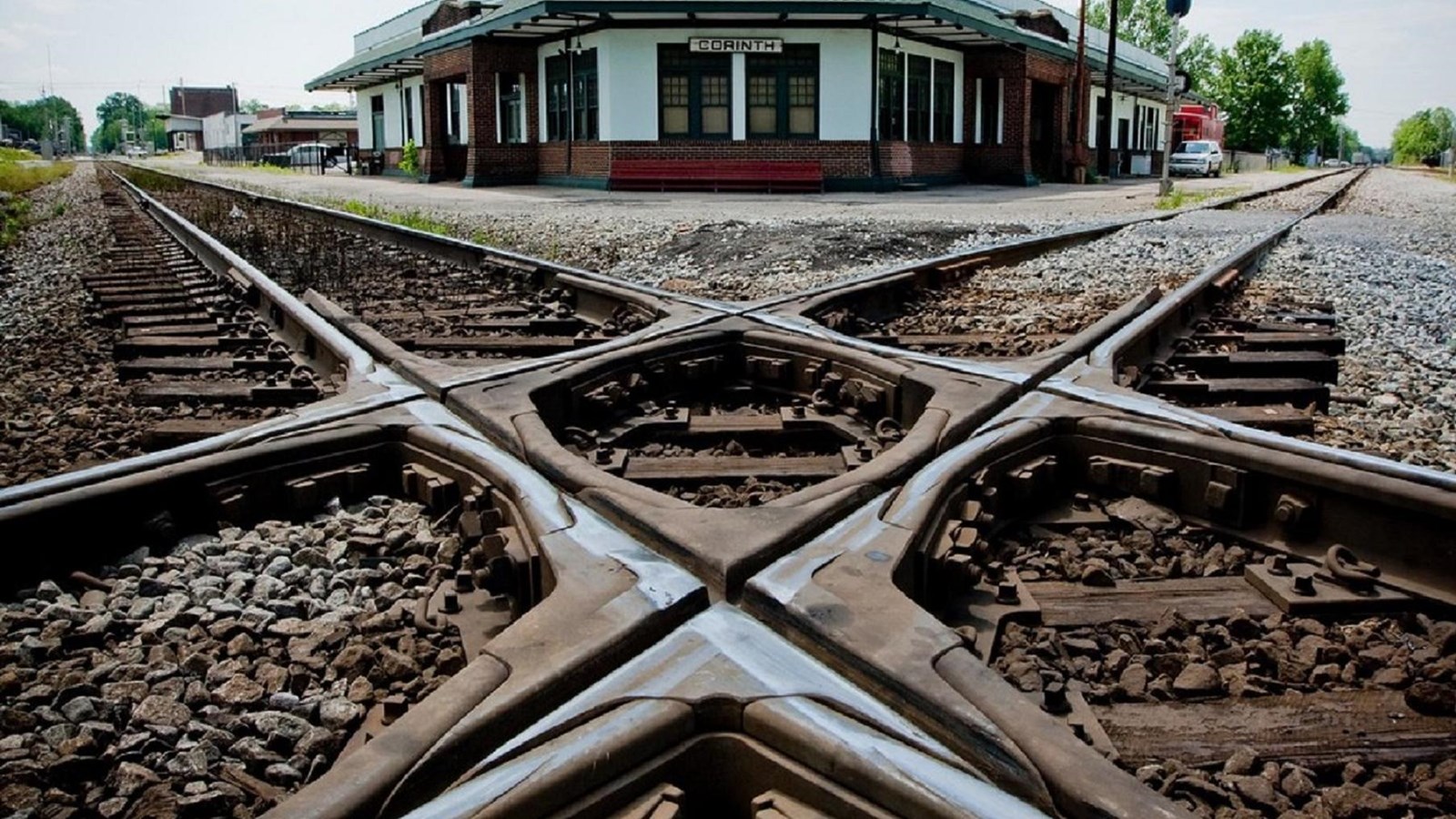 Image of two rail tracks crossing one another with a rail station in the background.