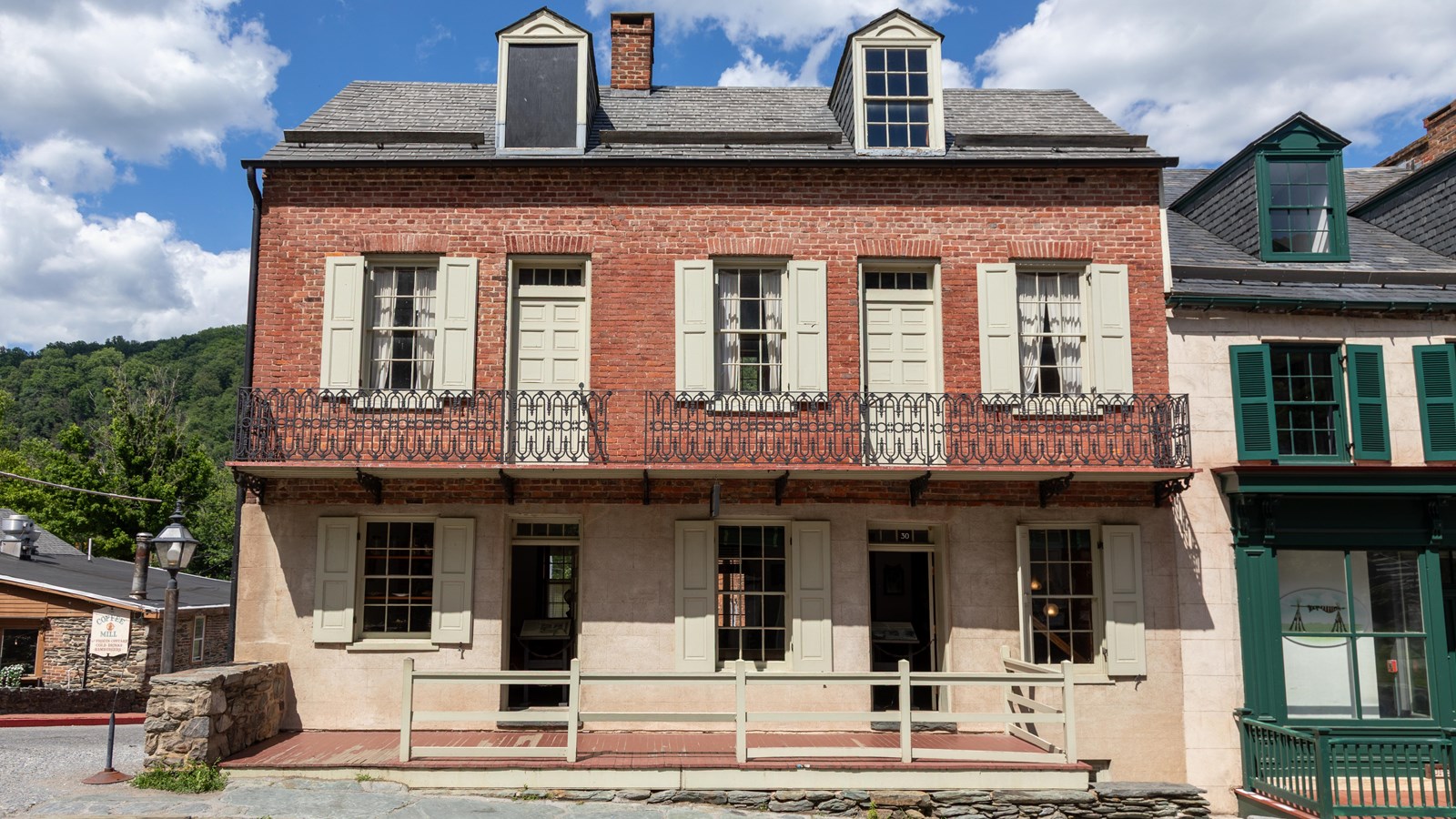 A three-story brick and stone building on a sloped street with a wooden porch and two open doors.
