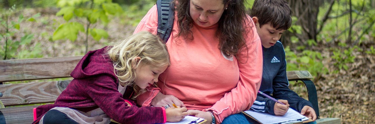 Mother and two children sitting on bench outside working on Junior Ranger book