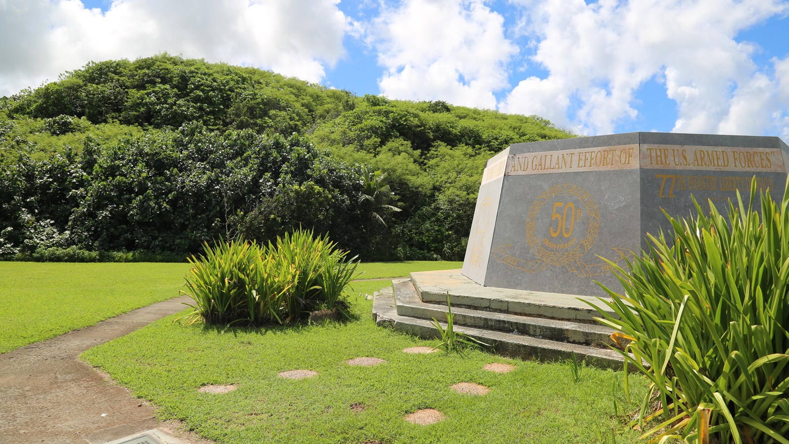 A low, six-sided concrete memorial. The side facing the camera says 