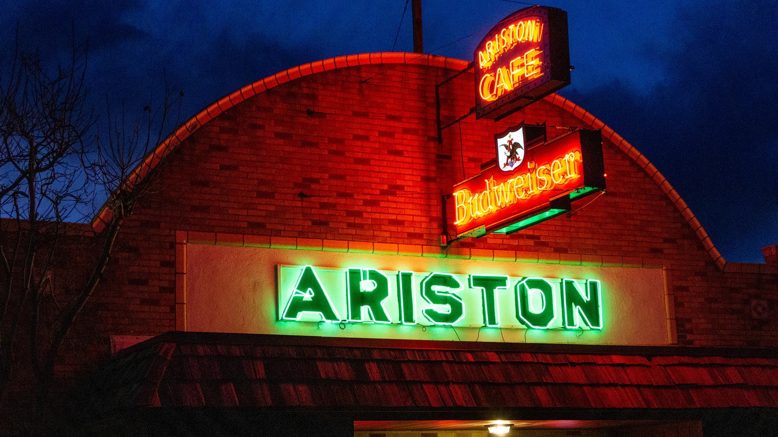 A brick building with a rounded roof with a green neon sign that reads