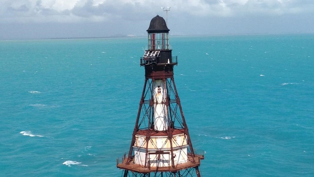 Aerial view of a skeletal metal lighthouse rising up over turquoise waters