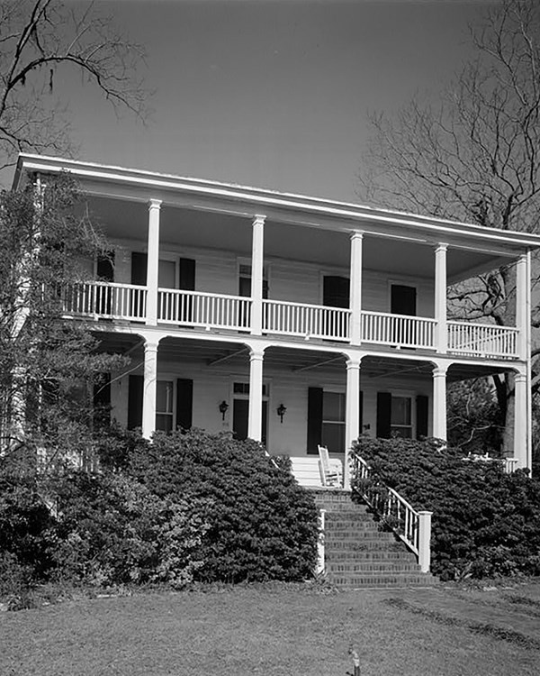 A large two-story house with a double porch and shutters on each window.