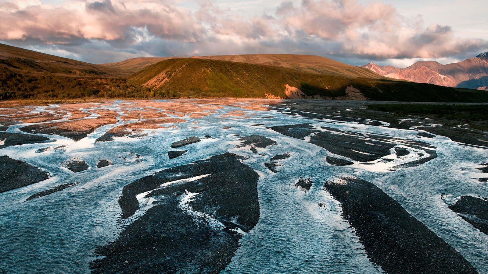 A braided river with channels of water and gravel bars stretches into the distance toward mountains.