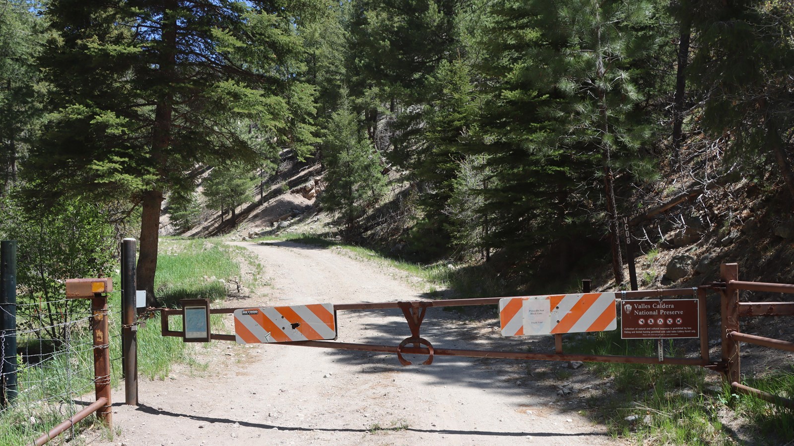 A large metal gate across a gravel road with a sign that says 