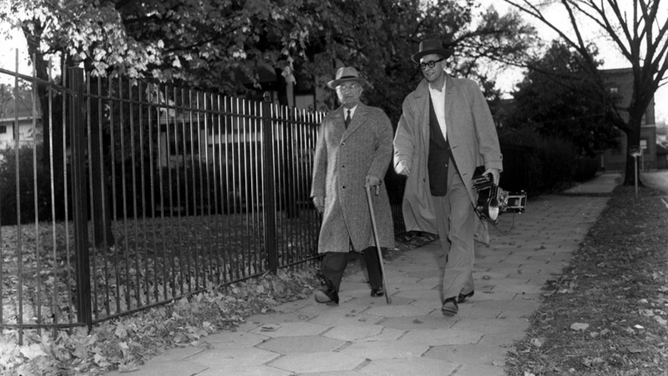 Harry S Truman, in coat and hat, with walking stick, walking.