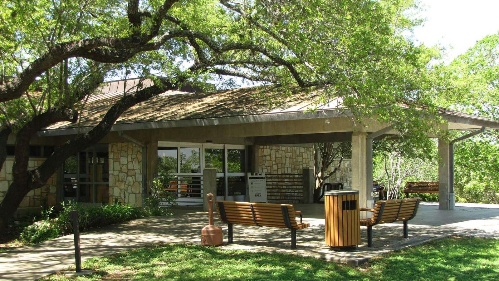 A wide portico extends from a building with sliding glass doors and outside benches.