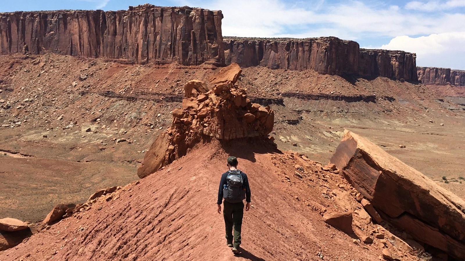 A hiker walks along a ridgeline towards Moses and Zeus Towers