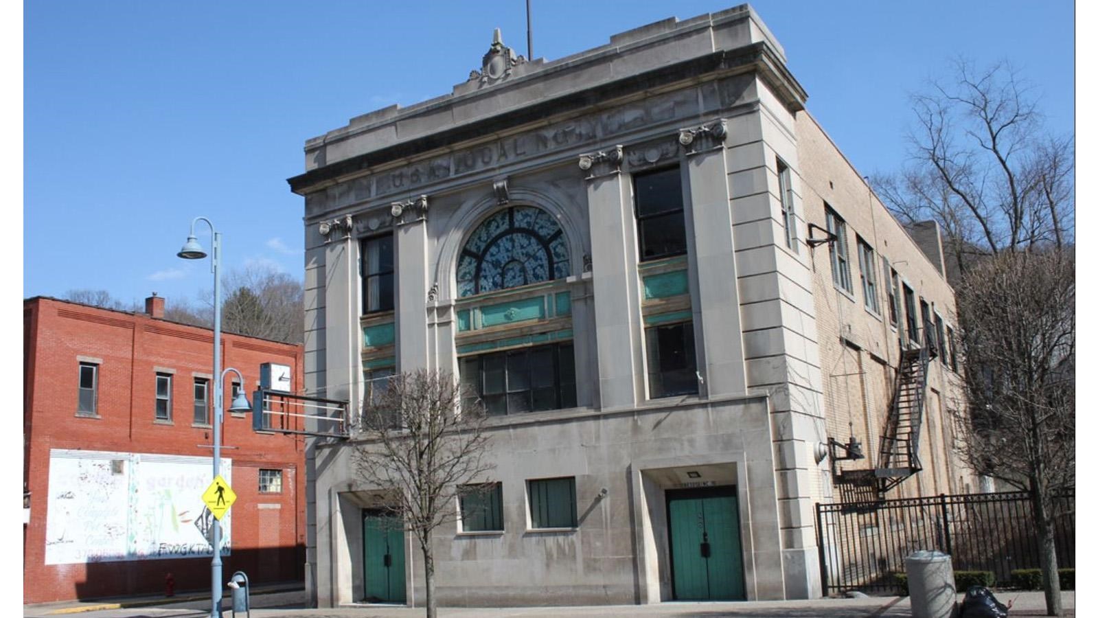 three story stone building facing the street with arched glass windows on the top floors  