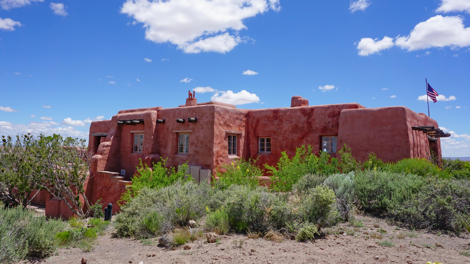 An orange adobe style building surrounded by grasses and shrubs.