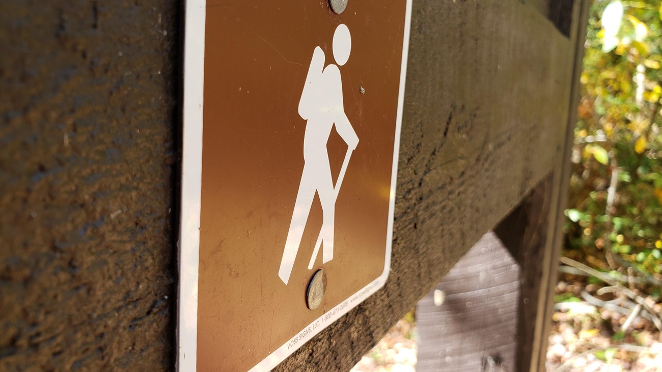 A brown sign up close on brown post with hiking emblem.