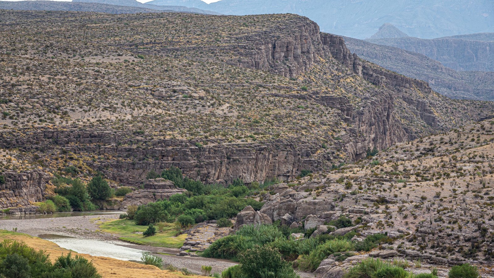 A river crosses an open plain before heading into a limestone canyon.