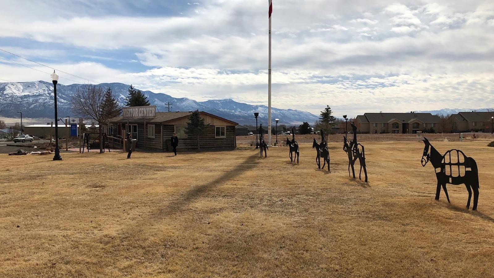 Silhouettes of a mule team in a grassy field next to a visitor center building.