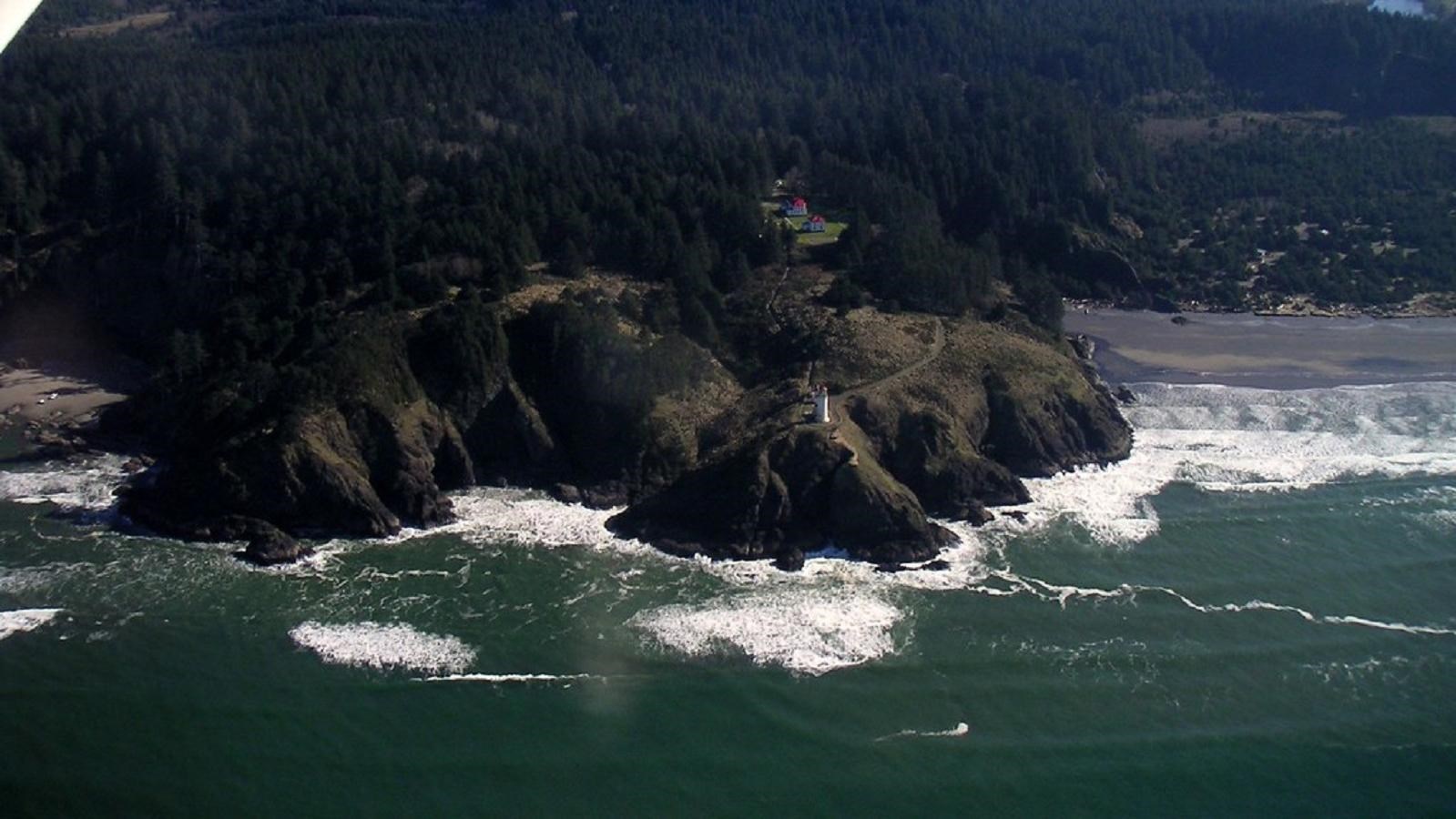 Ocean waves crash against a rocky cliff below a lighthouse
