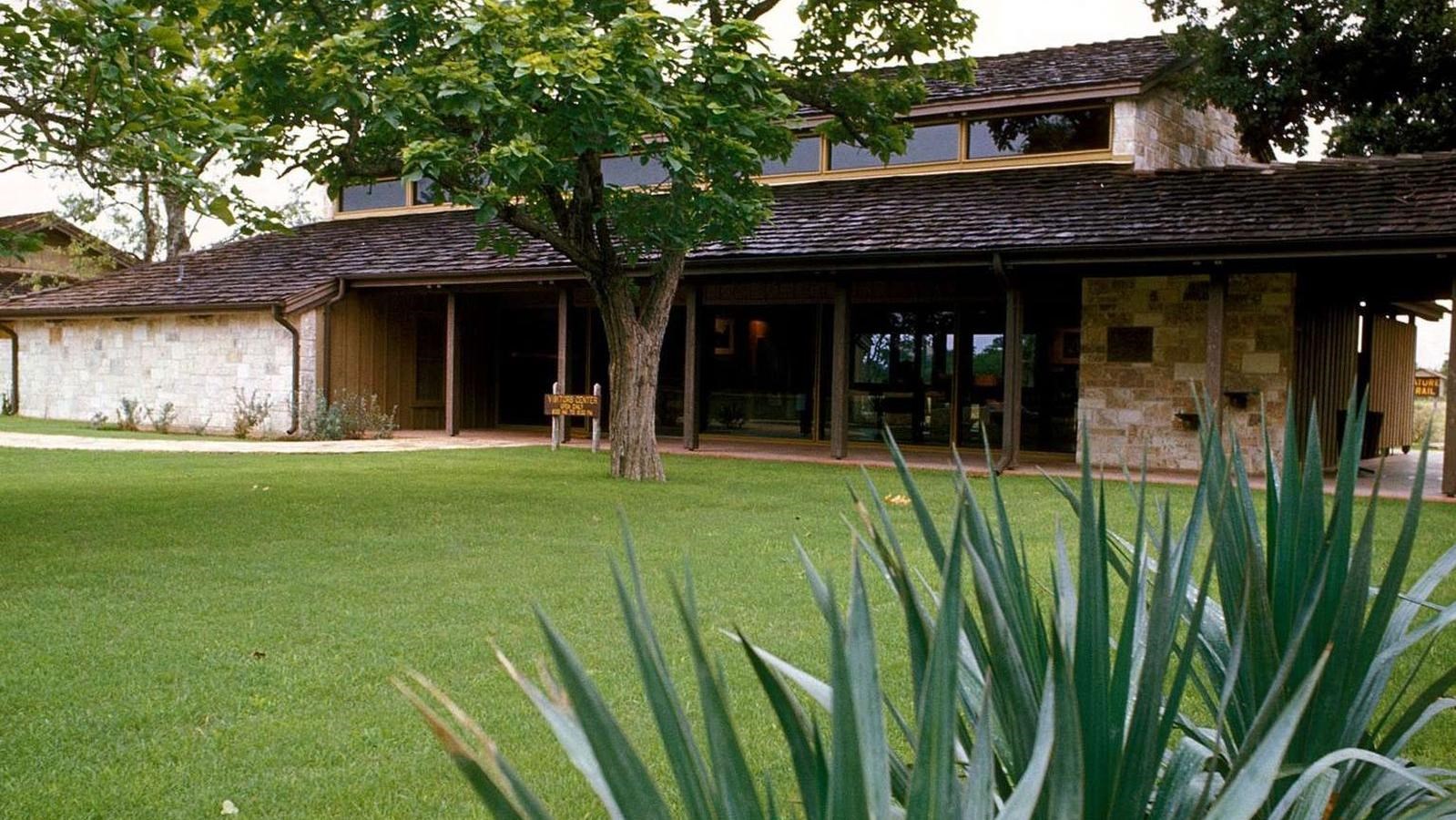 Beyond yucca plants, a stone structure with wooden shingles stands, fronted by a green lawn.
