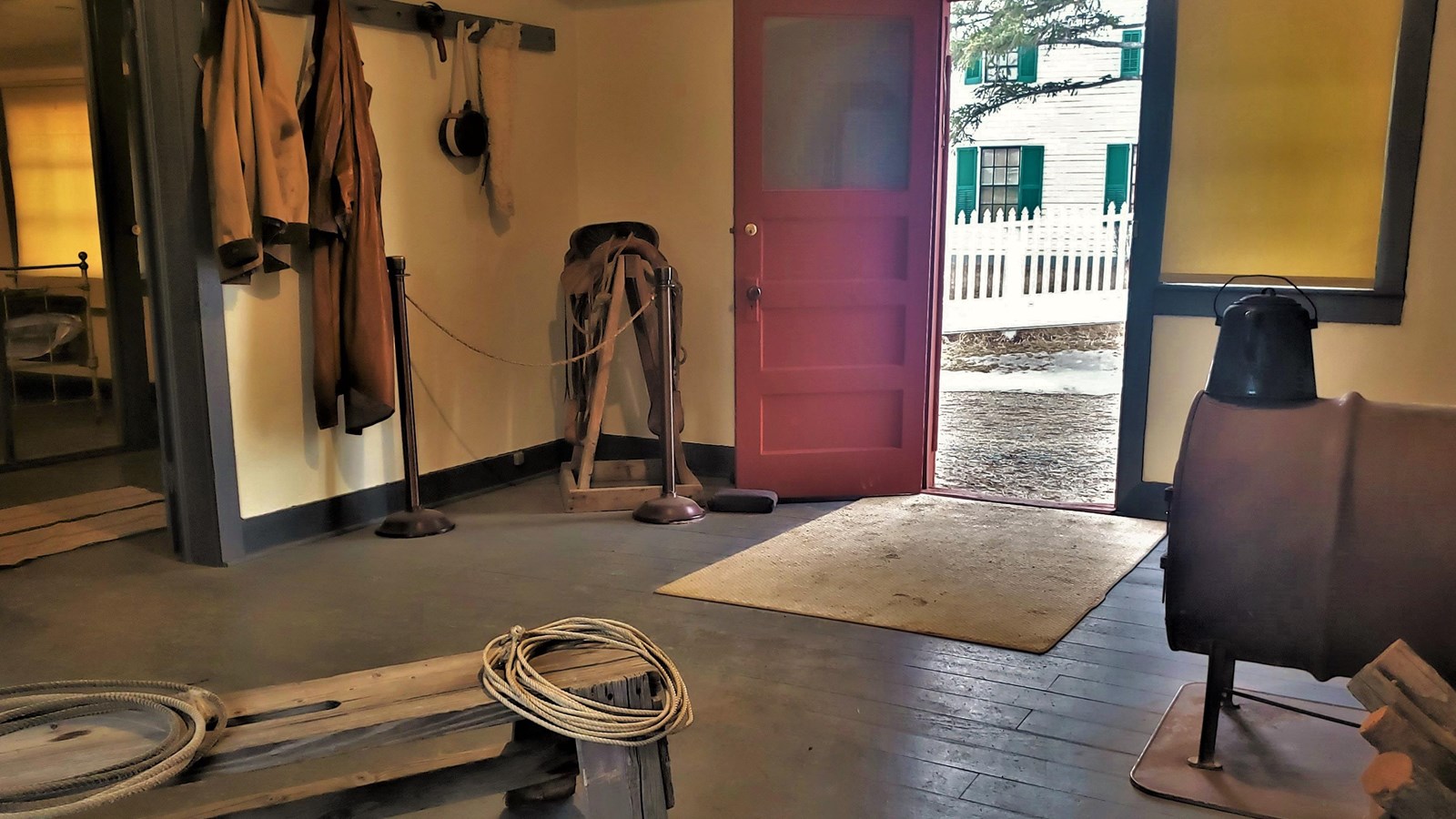 A small stove, lariats, saddle, and jackets are on display in the bunkhouse sitting room.