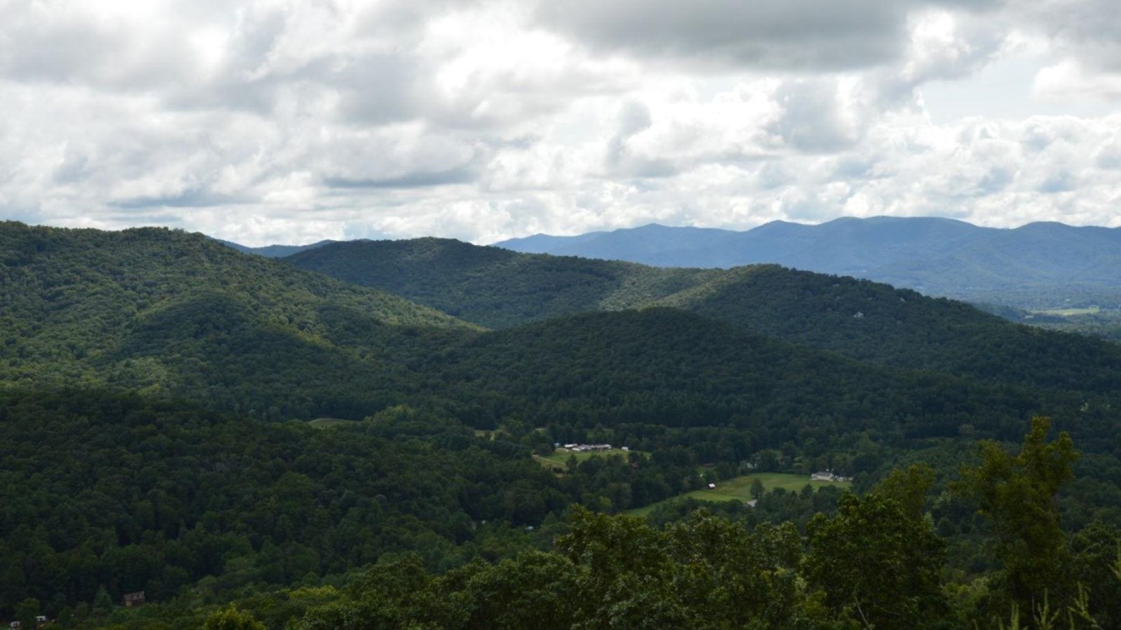 Forested valley spans out across the foreground with layered mountains in the distance