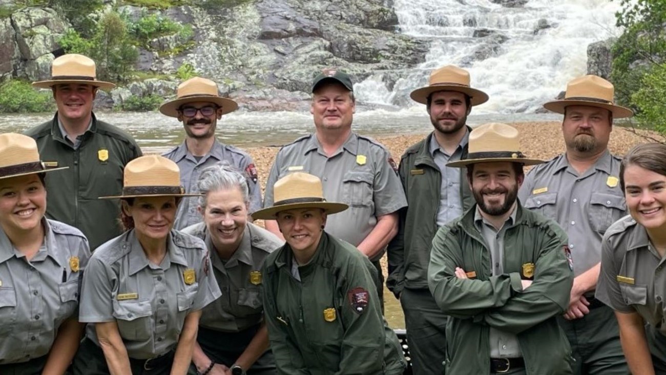 A group of National Park Service Rangers in uniform posing for a picture with a waterfall behind