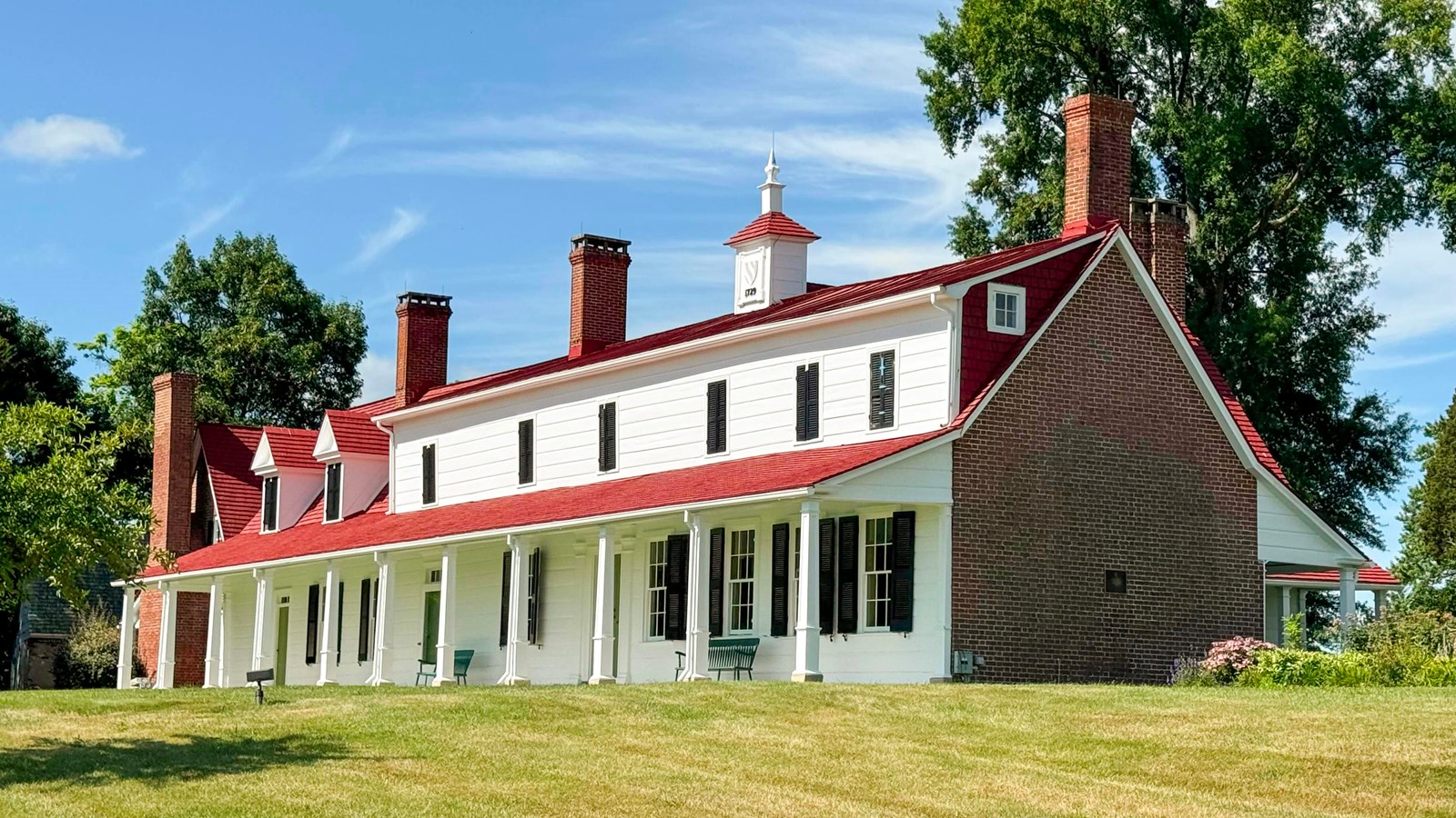 Historical house with white siding and a red roof on a sunny day.