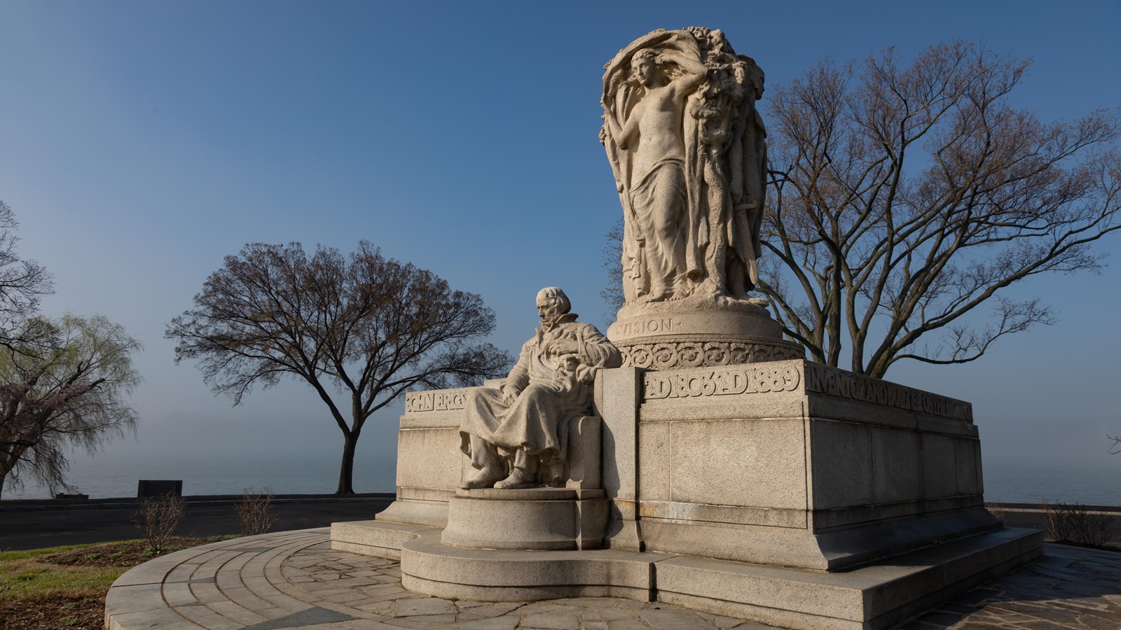 A stone statue of a man sitting with a river in the background. 