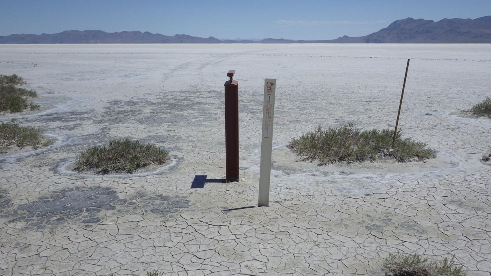 Salt plain with cracked earth and faint wagon tracks lead toward distant blue mountains.