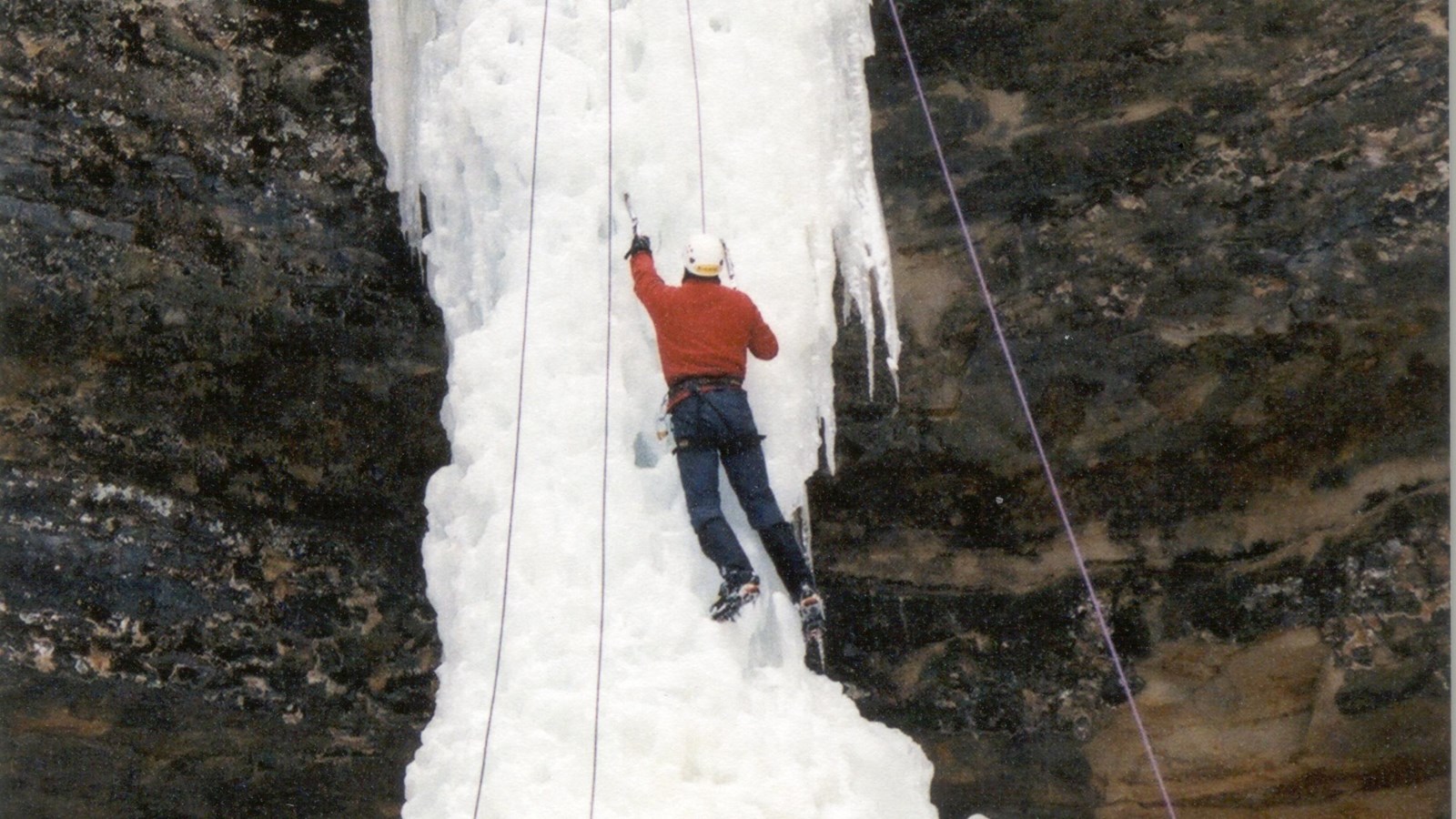 Ice climber half-way up a 50-foot high column of ice on cliff