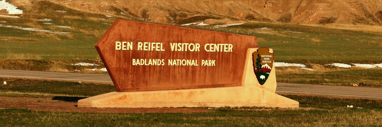 a sign reading ben reifel visitor center sits in front of jagged badlands formations.