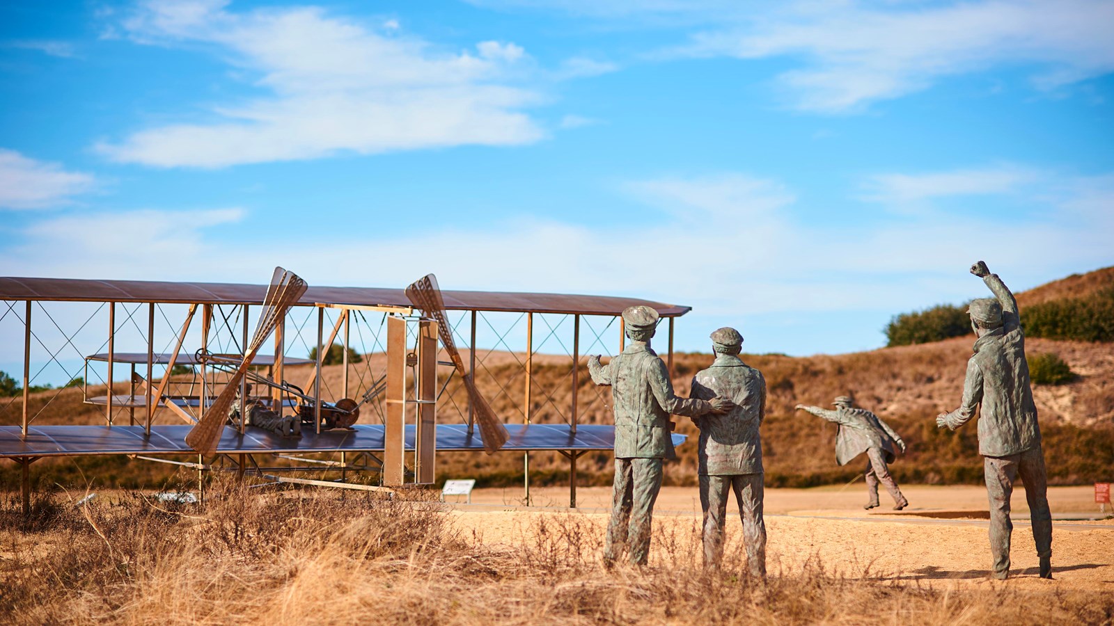 Bronze sculptures of 4 men stand next to a flyer as it appears to take off to the left.