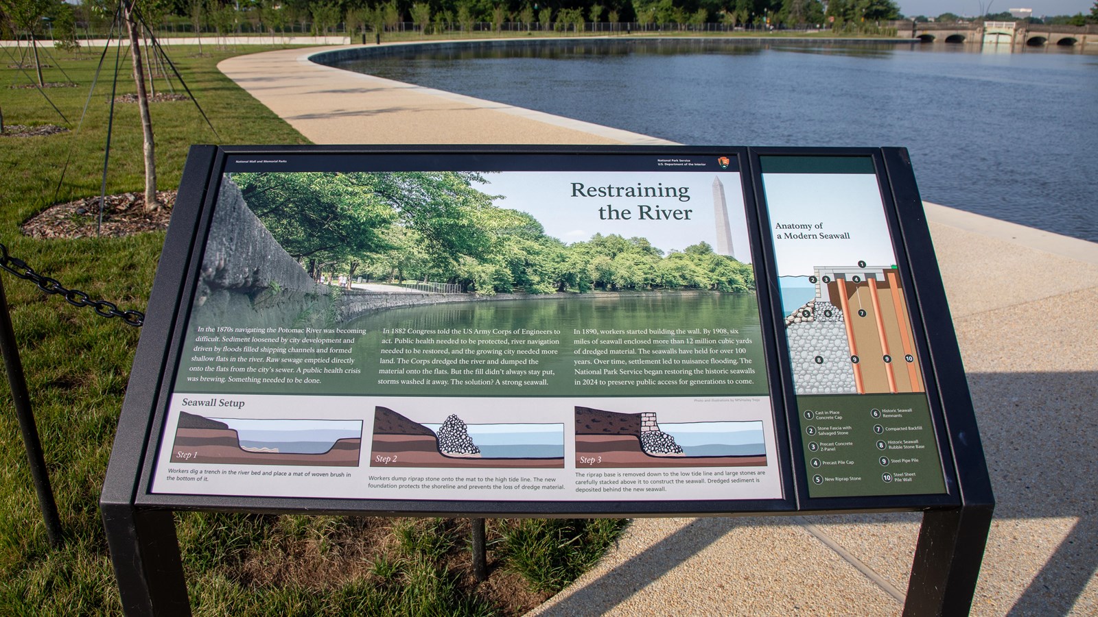 An information sign on black metal posts next to a sidewalk along a body of water.