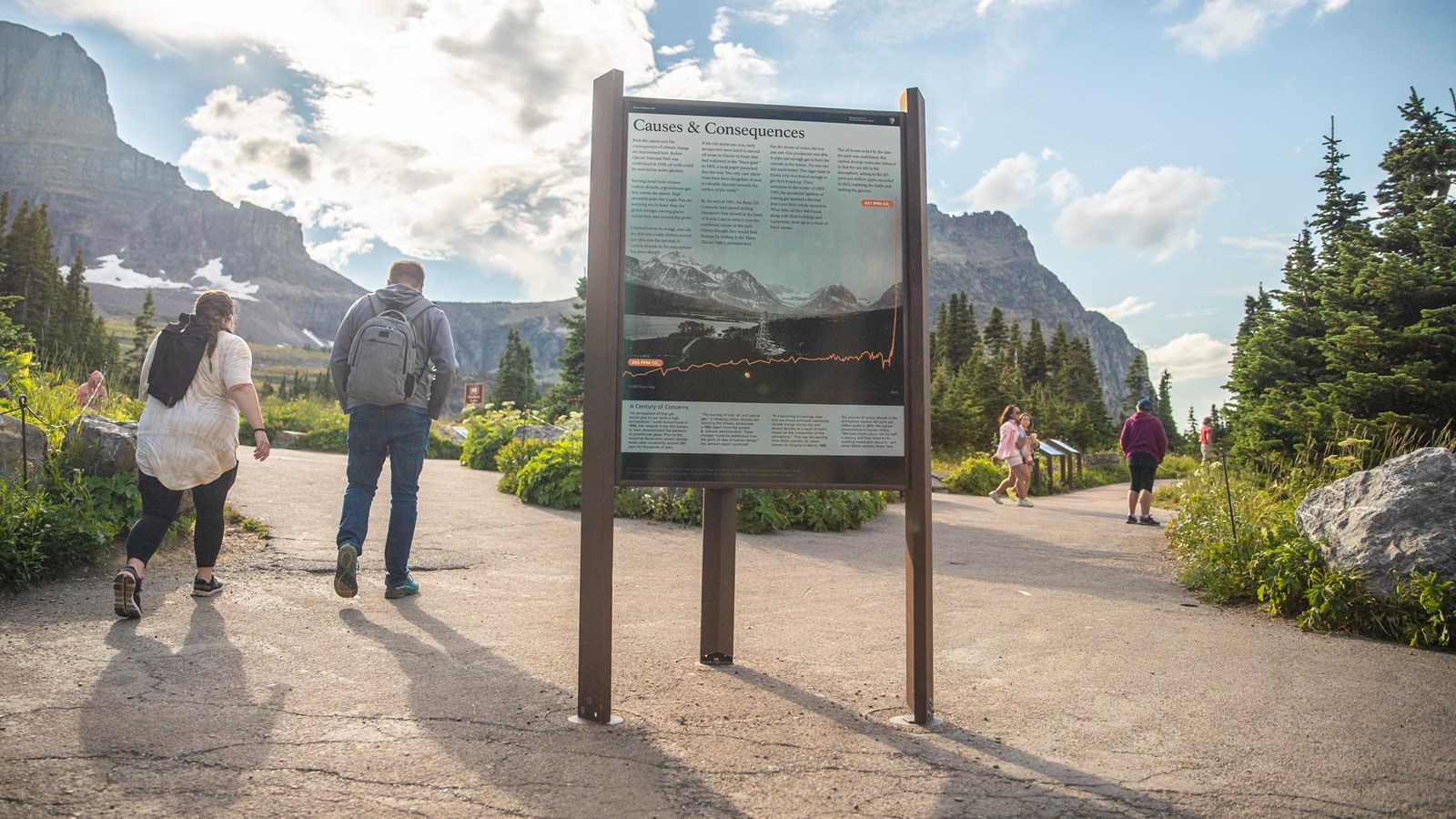People walk around a tall educational exhibit with mountains and clouds in the background.