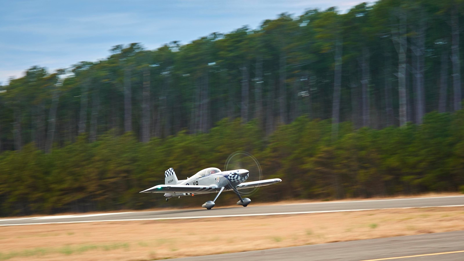 A small plane with blue and white checkerboard on the tail and nose is in motion, taking off.