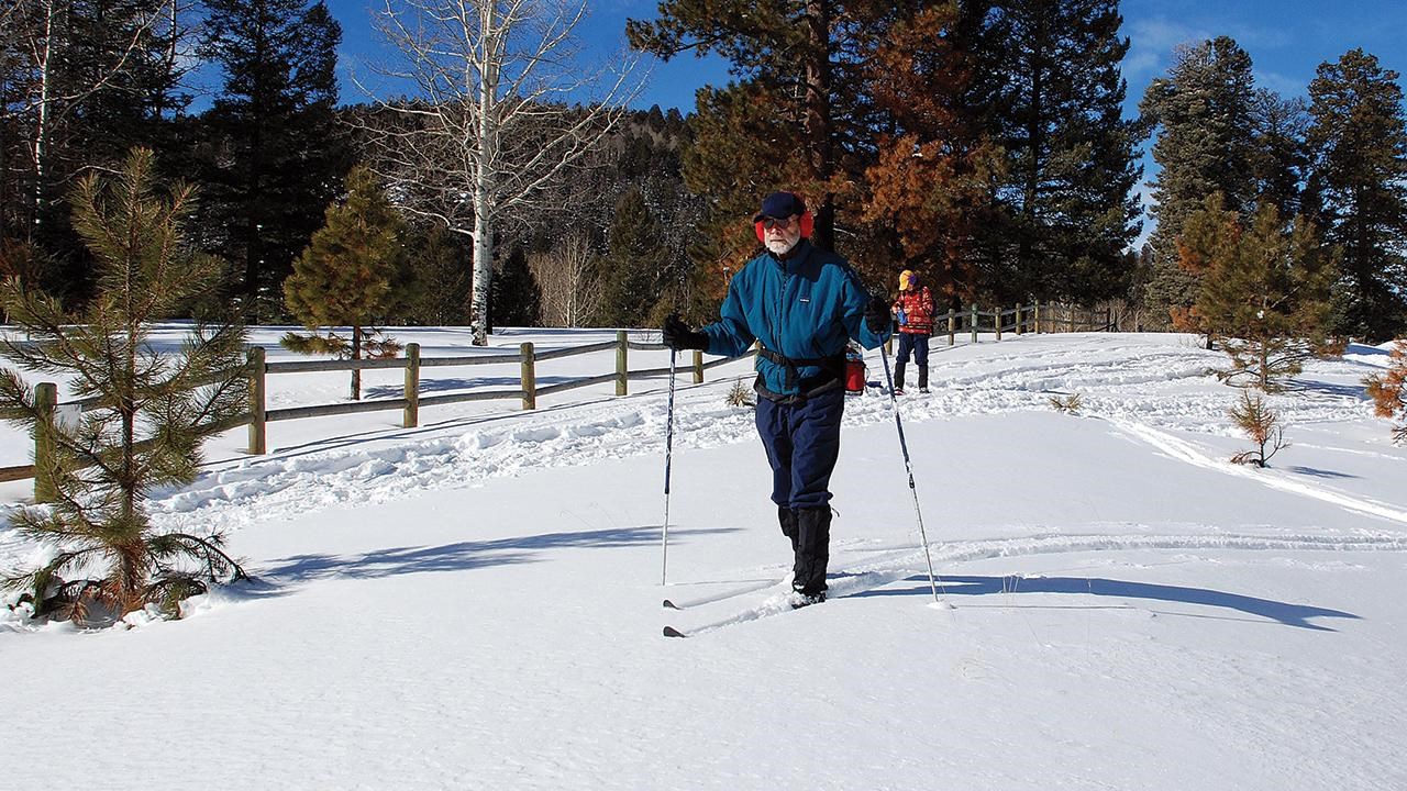 Man cross-country skis on a snowy mesa.