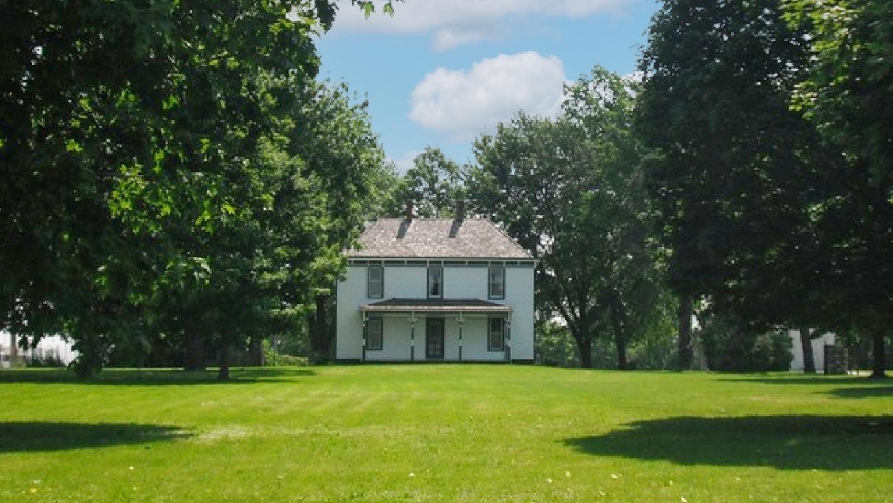 Large cream color farm home with green trim, grass and trees