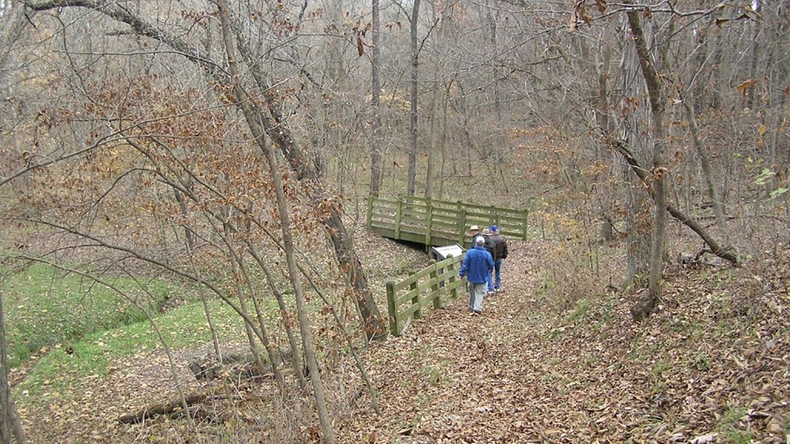 Bridge over Salt Creek featuring a wayside exhibit in a heavily wooded area.  