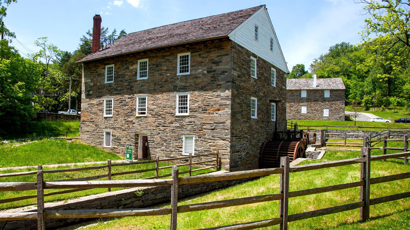 A three story brick house with several windows. A mill is next to it, and a fence surrounds both the