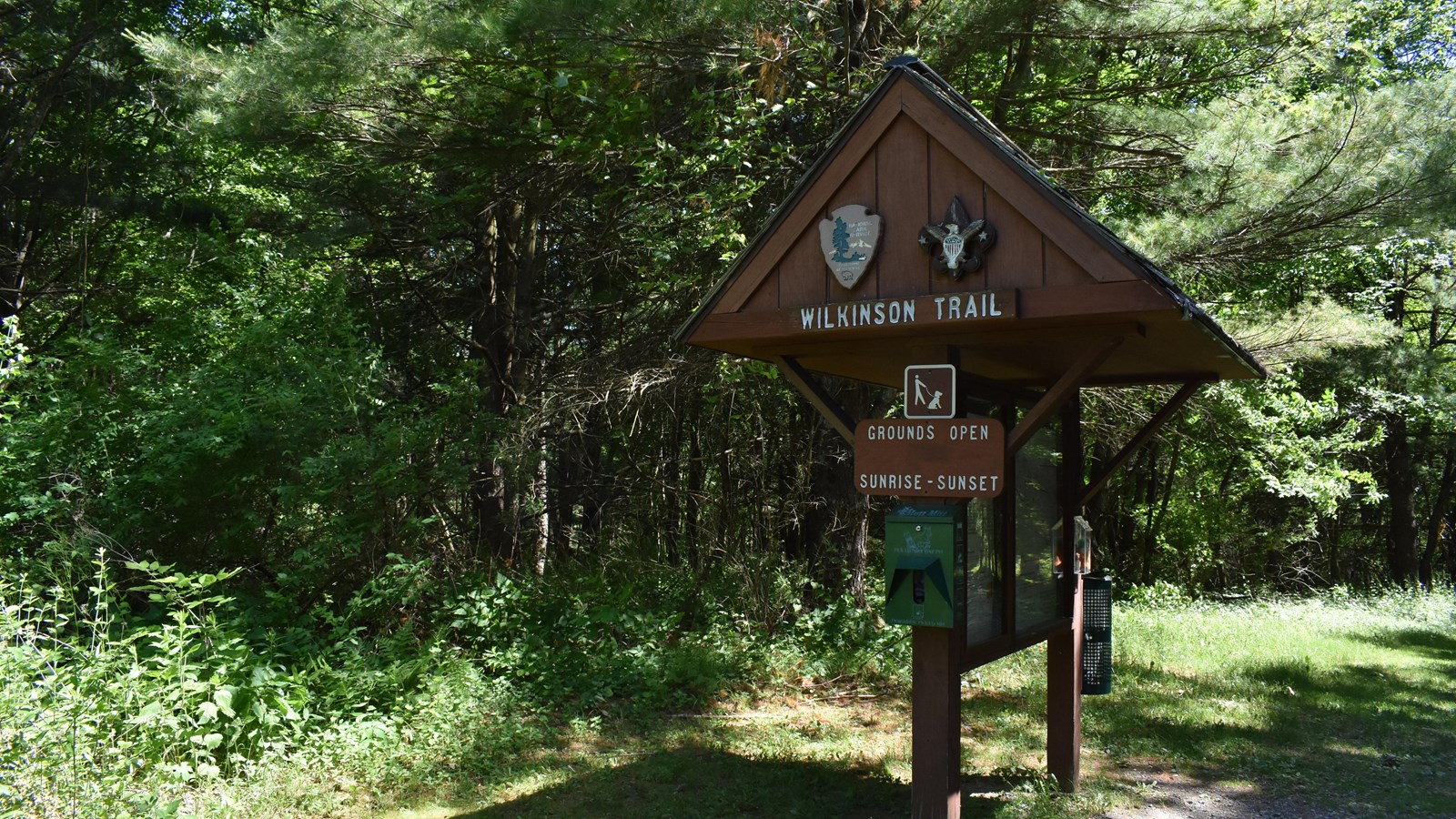 A Large roofed notice board marked Wilkinson Trail, surrounded by bright green trees