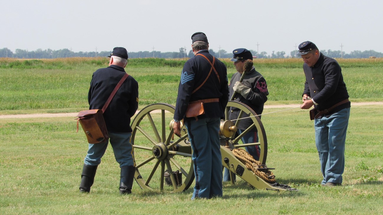 Men in 19th century U.S. Army uniforms prepare to fire a cannon.