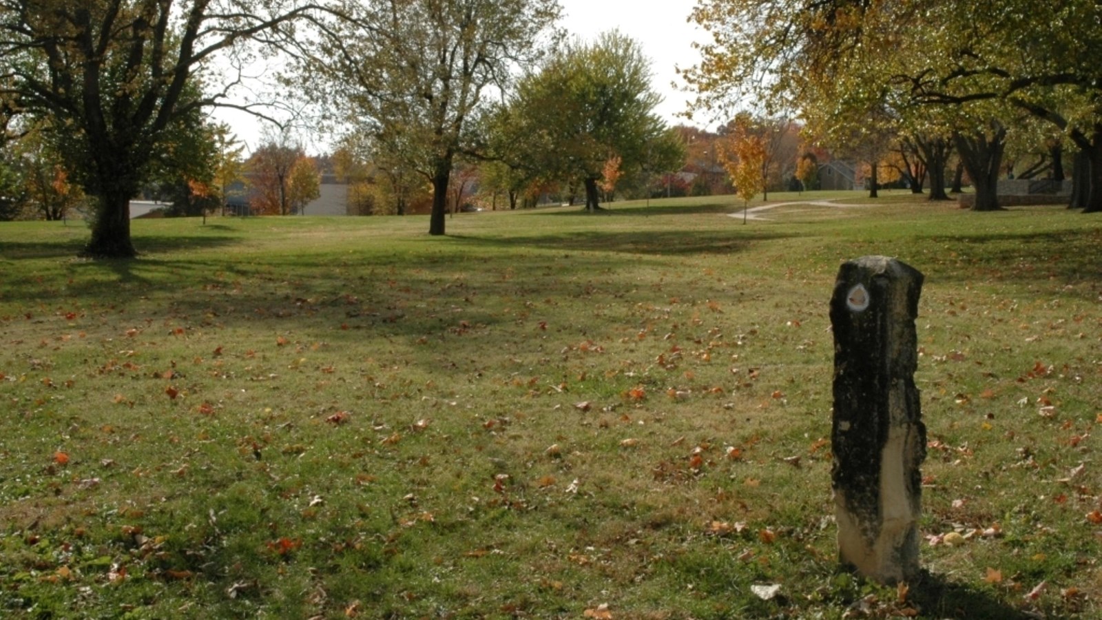 A stone marker sits in front of a grassy park dotted with distant trees.