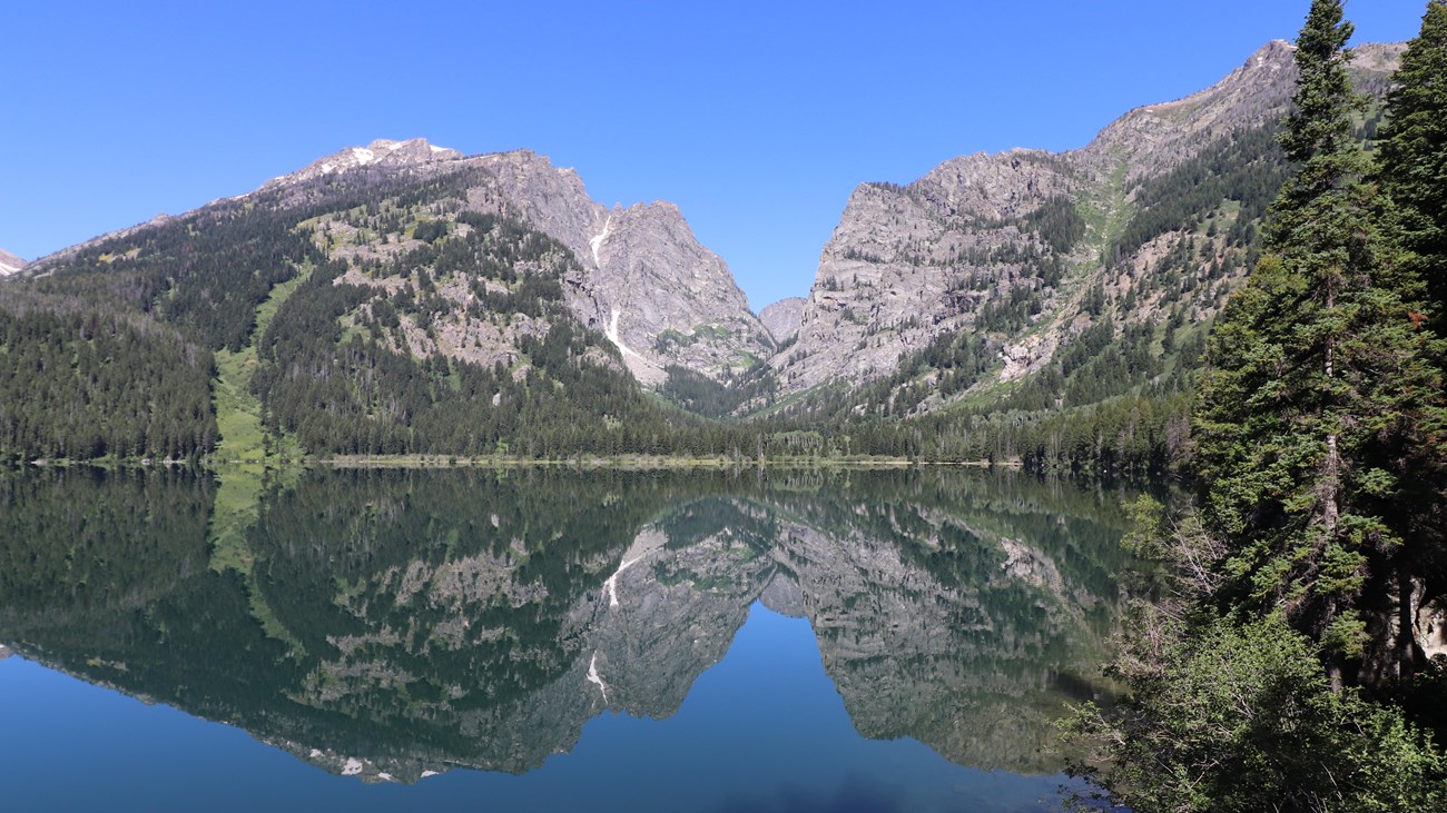 A lake sits at the base of a mountain canyon with a near perfect reflection on its calm surface.