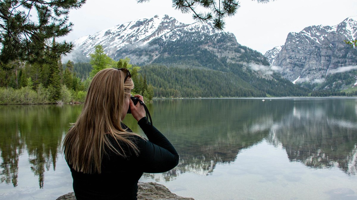 A woman takes a picture beside a lake.