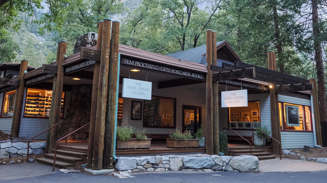 A covered porch with exposed log beams leads to a warmly lit rustic building