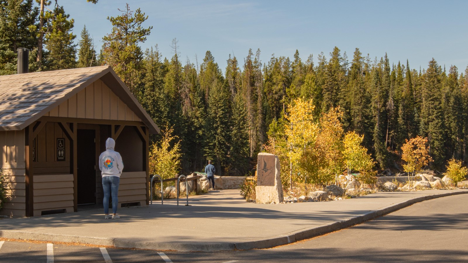 A restroom on the left of the page with a person waiting and a small plaza with trees.