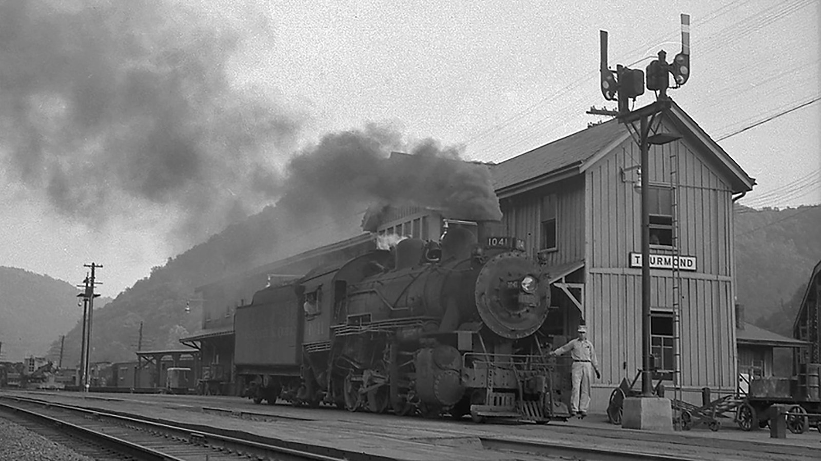 Old picture of a large steam locomotive and engineer in front of a wooden train depot