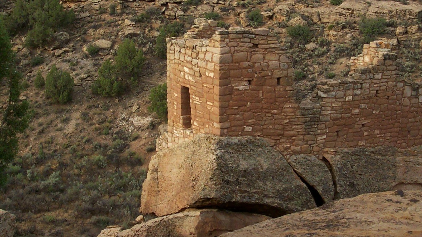 remains of a rectangular stone structure perched on a boulder next to the canyon rim. A doorway face
