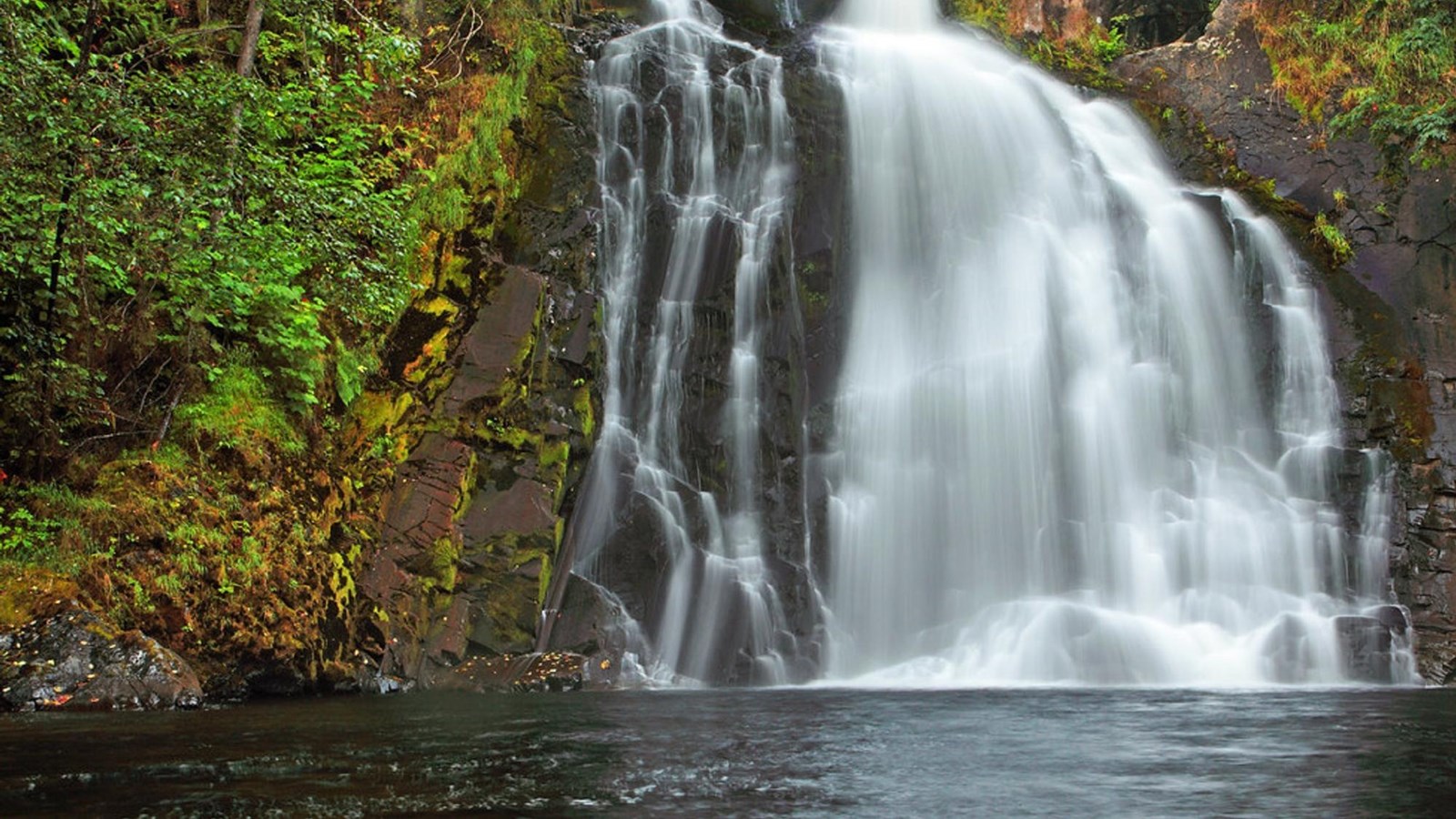 Water cascades over a cliff to a tree-lined pool below.