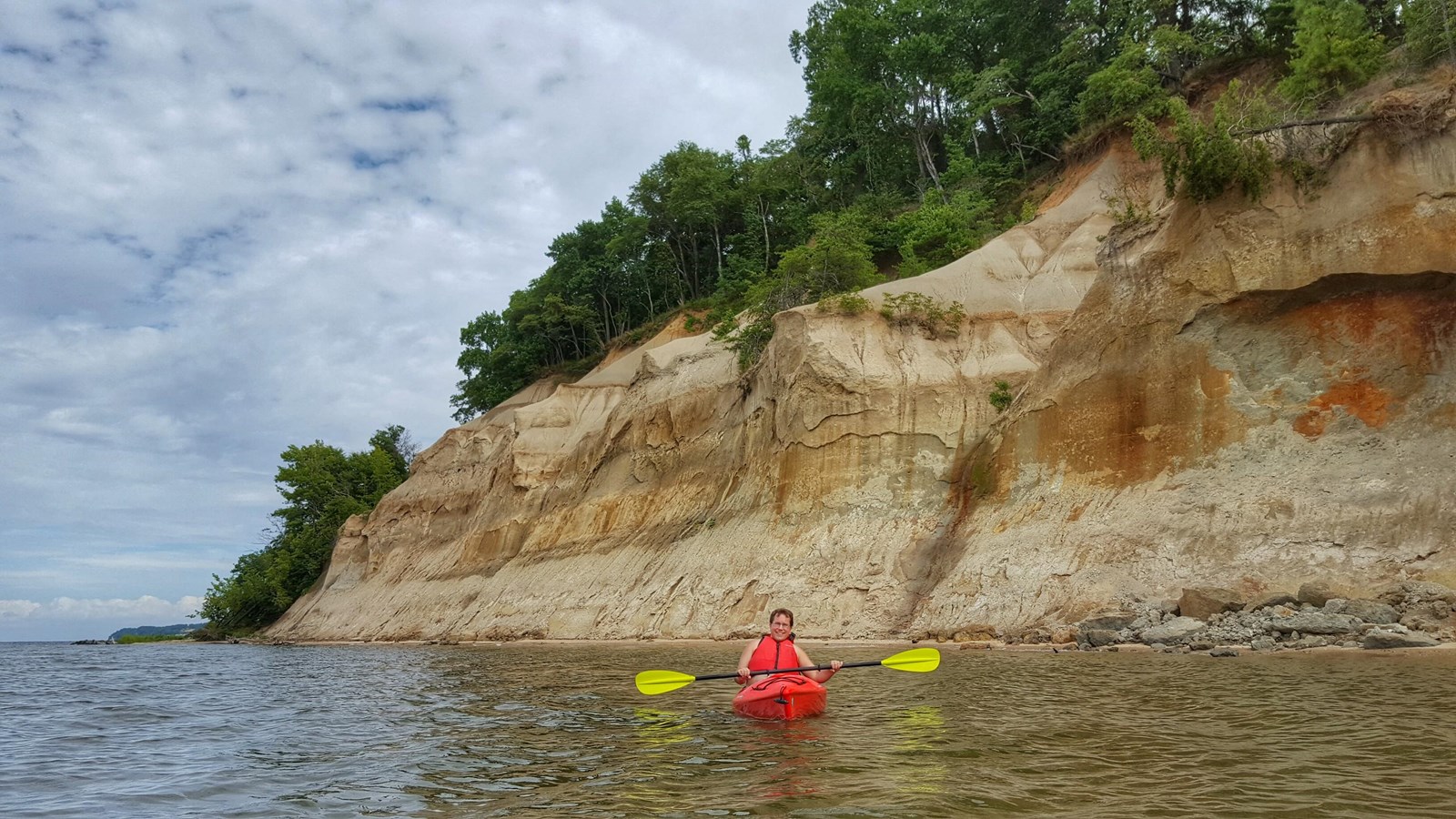 A tall exposed cliff on the riverside with a kayaker below. 