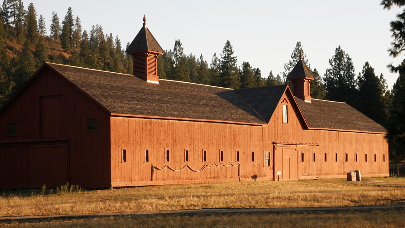 Long wood building with brown shingles and two small towers sits in a dry grassy field.