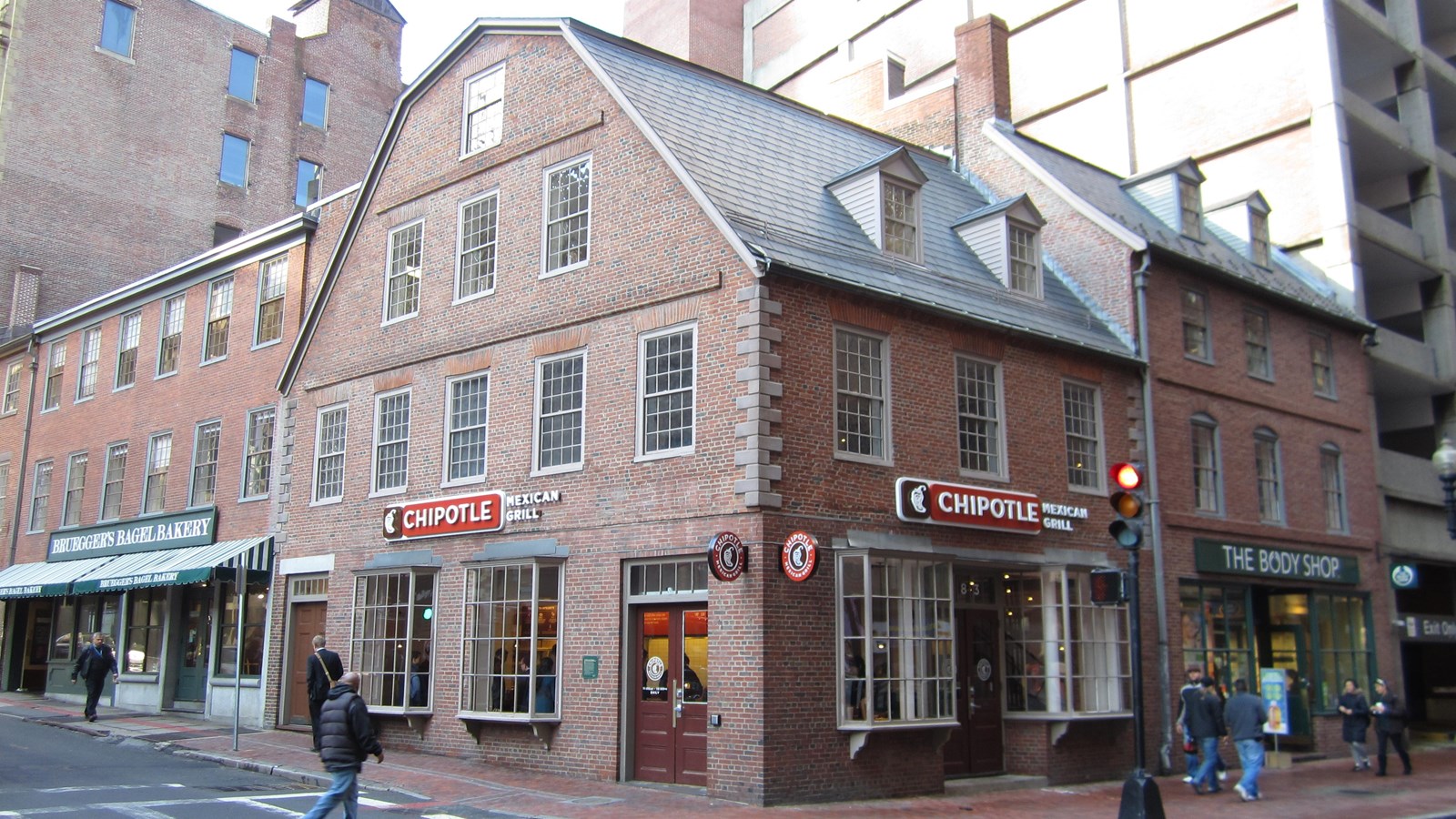 Photograph of a brick three story building under a gambrel roof. Signs read Chipotle